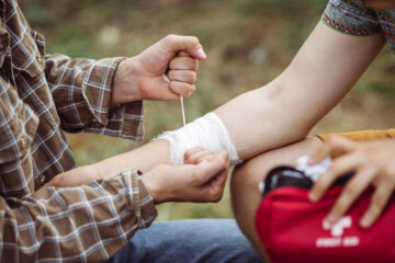 A person wrapping his friends injured arm in gauze from a first aid kit.